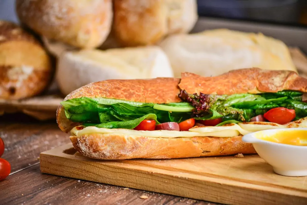 Sandwich on a cutting board with rolls in the background. Photo by Raphael Nogueira on Unsplash