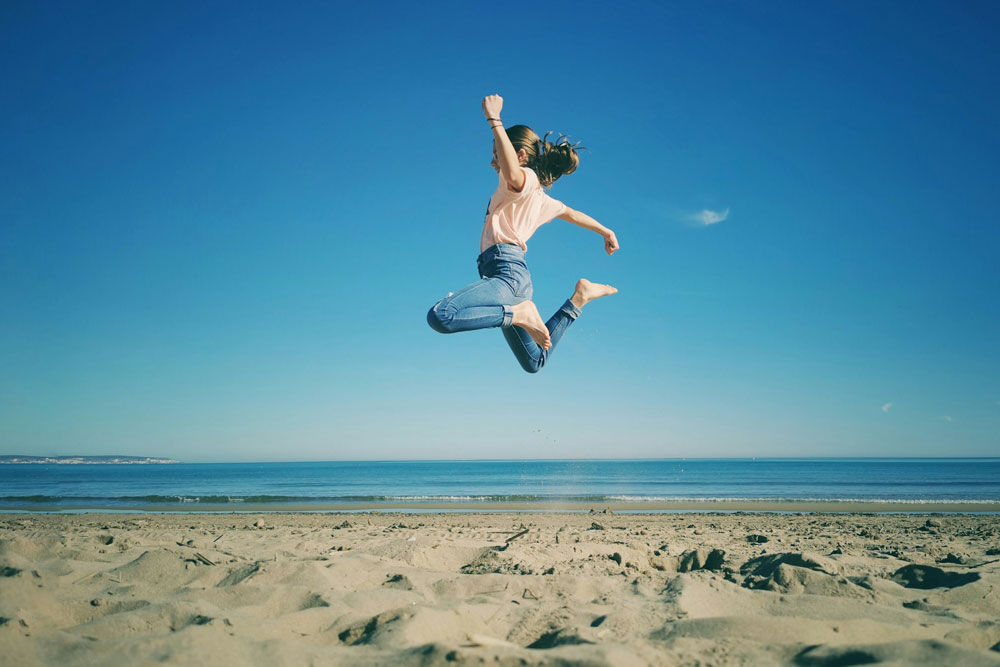 A girl at the beach jumps for joy in midair. Photo by Vultar Bahr on Unsplash.