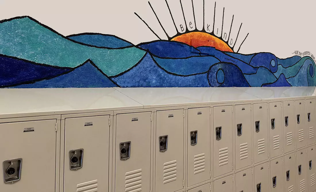 Interior of PGMS hallway with tan lockers and a mural of ocean waves and a sun with the words Be Kind