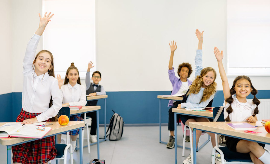 A group of smiling students in a classroom raising their hands. Photo by Yan Krukov on Pexels.
