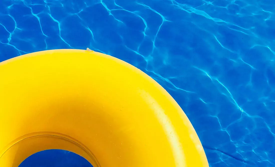 A yellow inflatable pool ring floats on a blue swimming pool. Photo by Evan Chen on Unsplash.