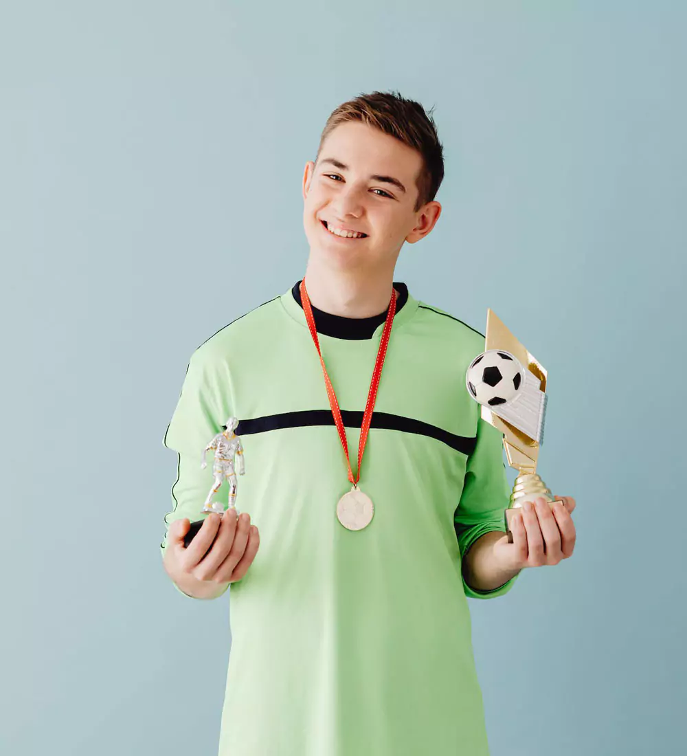 Young man holding 2 trophies with a medal around his neck and smiling at the camera. Photo by Karolina Grabowska on Pexels