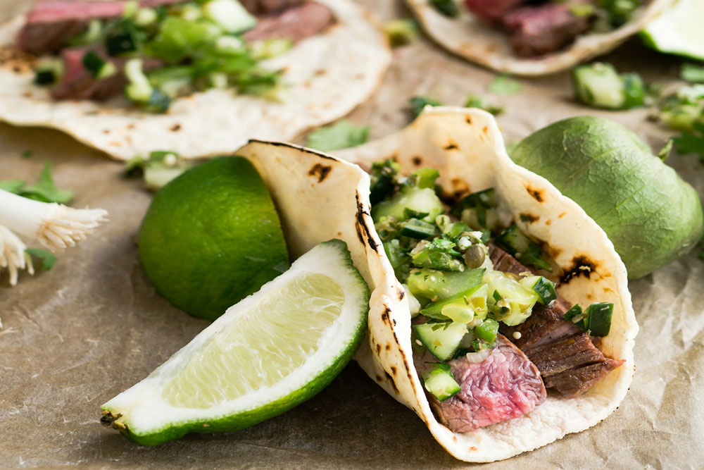 Close up of Mexican Street Tacos with beef, onions, guacamole and lime in a corn tortilla. Photo by Christine Siracusa on Unsplash.