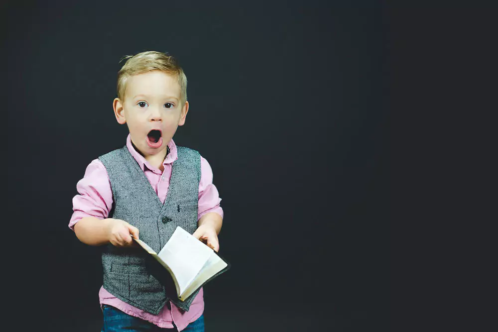 A small boy singing at the top of his lungs and holding a choir book. Photo by Ben White on Unsplash.